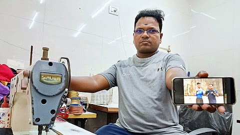 M Suresh Babu poses with a picture of him and his son Vishvanath and a sewing machine in his tailoring shop in Kolathur