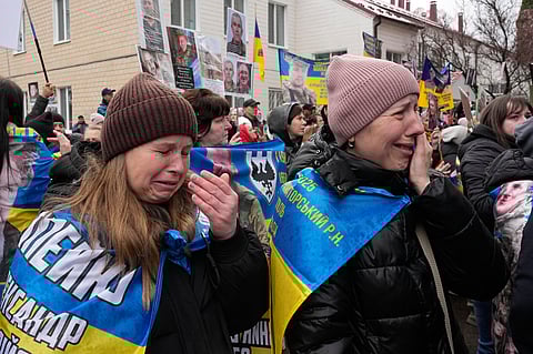 People cry as they hold hold photos of their missed relatives as Ukrainian soldiers return from captivity during a POW exchange between Russia and Ukraine in Chernyhiv region, Ukraine, Saturday, April 11, 2026.