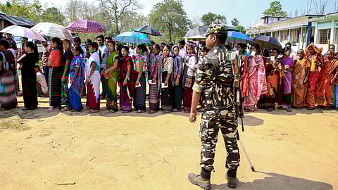 A security personnel stands guard as voters wait in queues to cast their votes during the Tripura Tribal Areas Autonomous District Council (TTAADC) elections, in the Dhalai district, Tripura, Sunday, April 12, 2026.