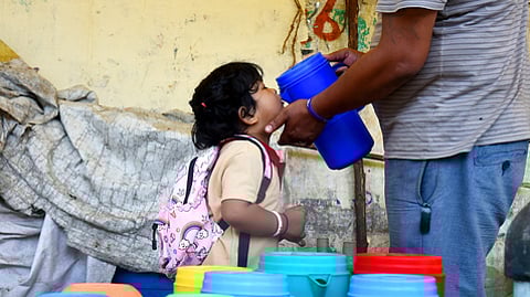 A father helps his daughter quench her thirst from a water flask as the summer heat intensifies