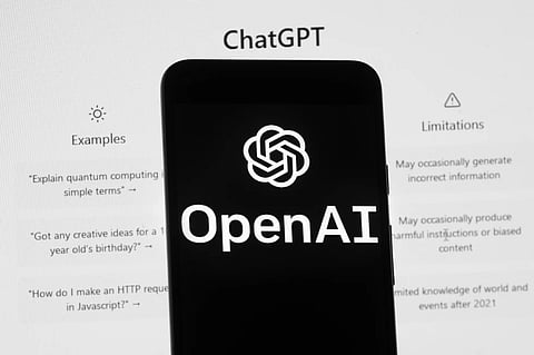 The OpenAI logo is seen on a mobile phone in front of a computer screen which displays the ChatGPT home Screen, March 17, 2023, in Boston.