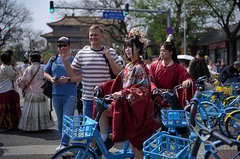 A foreign tourist poses next to a Chinese couple dressed in imperial costumes near the Forbidden City, in Beijing, on Sunday, April 12, 2026.