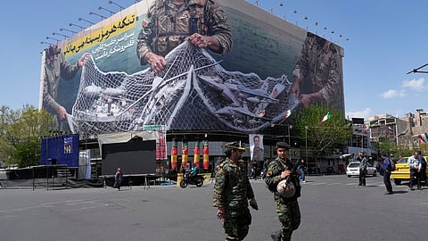 FILE - Two police officers walk in front of an anti-U.S. billboard depicting American aircraft being caught by Iranian armed forces in a fishing net beneath the words in Farsi, "The Strait of Hormuz will remain closed, The entire Persian Gulf is our hunting ground," in Tehran, Iran, Sunday, April 5, 2026.