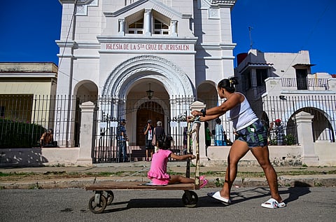 A woman pushes a cart with her daughter past the Church of the Holy Cross of Jerusalem in Havana on April 14, 2026.