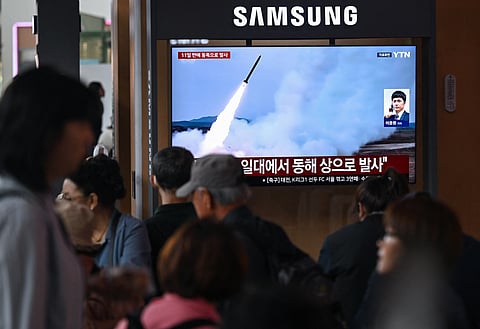 People watch a television screen showing a news broadcast with file footage of a North Korean missile test, at a train station in Seoul on April 19, 2026.