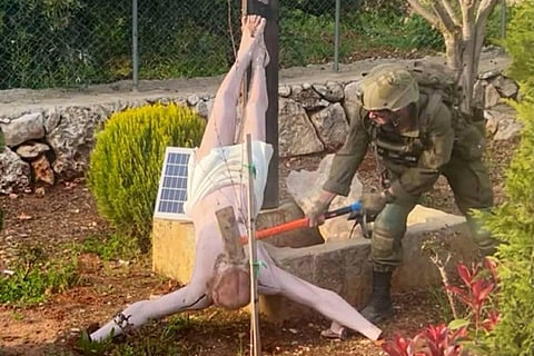The image appears to show an Israeli soldier using a sledgehammer to strike the head of a statue of a crucified Jesus that had fallen off of a cross.