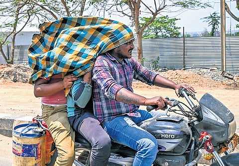 Men, triple riding a bike, cover their face with a towel to escape the intense heat conditions, near Patia in Bhubaneswar on Thursday