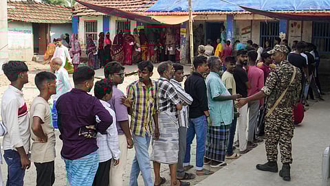 A security official stands guard as people wait in a queue to cast votes during the first phase of the West Bengal Assembly election, in Nandigram, Purba Medinipur district, Thursday, April 23, 2026.