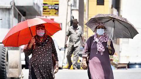 Women use portable shade under an umbrella while navigating the city streets during an intense afternoon heatwave.