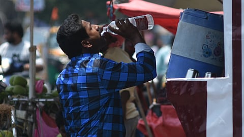 A man quenches his thirst as he drinks water from a kiosk on a sunny afternoon in Vijayawada.