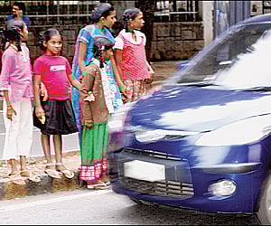 Pedestrians wait on a divider to cross the road| EXPRESS PHOTO