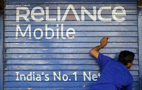 A man opens the shutter of a shop painted with an advertisement of Reliance Communications in Mumbai. | File/Reuters