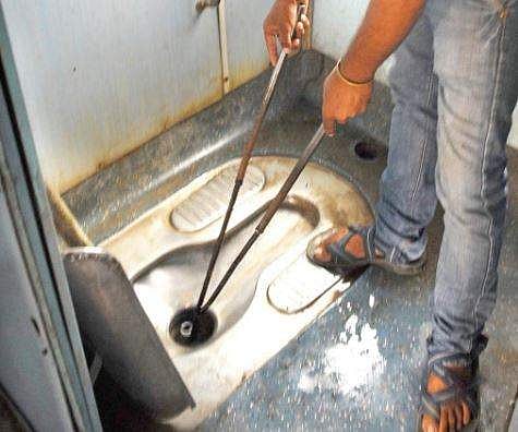 A worker using a garbage picking tong to clear a clogged bio-toilet on a train | (D Sampath Kumar | EPS)