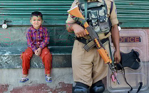 A boy looks on as a security jawan stands guard during curfew and srike in Srinagar for 15th consecutive day on Sunday. | (File Photo/PTI)