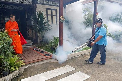 A city worker fumigates the area to control the spread of mosquitoes as a Buddhist monk looks on at a temple in Bangkok | Reuters