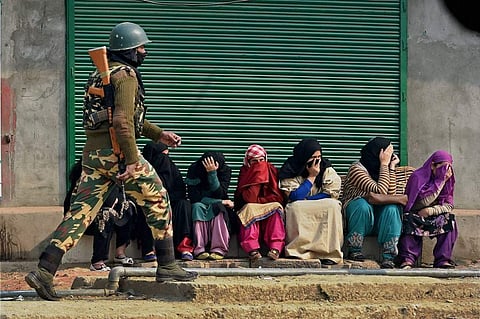 A soldier walks past women sitting outside a shuttered shop in Kashmir, where unidentified attackers burned schools amid protests that erupted after the death of the militant Burhan Wani (Photo | PTI)