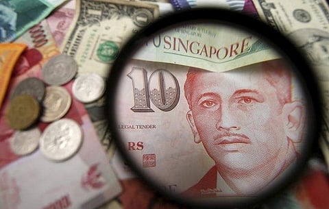 Singapore currency notes are seen through a magnifying glass among other currencies. | Reuters