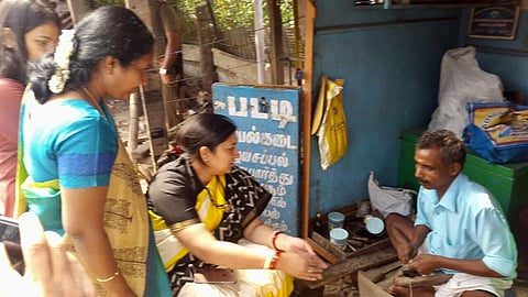 Union Minister Smriti Irani mends her sandal at a cobbler shop near Coimbatore during her visit to city on Saturday.  | EPS