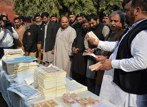A Pakistani police official (R) displays fake currency notes next to men arrested during a raid on a factory making counterfeit money in Lahore on February 25, 2016. | AFP