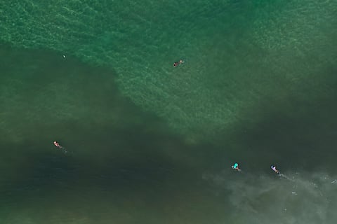 This July 5, 2016 photo, shows an aerial view of surfers paddling into the polluted waters off Sao Conrado beach in Rio de Janeiro, Brazil. | AP