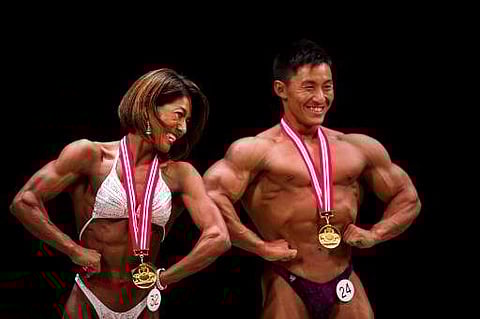 In this picture taken on October 9, 2017, winning Japanese bodybuilder in the women's category Megumi Sawada and winner in the men's category Masashi Suzuki pose on stage during the Japan bodybuilding championships in Tokyo. | AFP