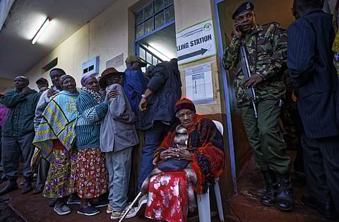 An elderly Kenyan woman takes a rest after casting her vote, while a policeman provides security, just after dawn in President Uhuru Kenyatta's hometown of Gatundu, Kenya on Oct. 26, 2017. (Photo | AP)