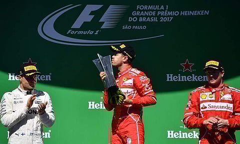 Ferrari's German driver Sebastian Vettel (C) kisses his trophy on the podium next to runner-up Mercedes' Finnish driver Valtteri Bottas (L) and third-place Ferrari's Finnish driver Kimi Raikkonen, after winning the Brazilian Formula One Grand Prix.|AFP