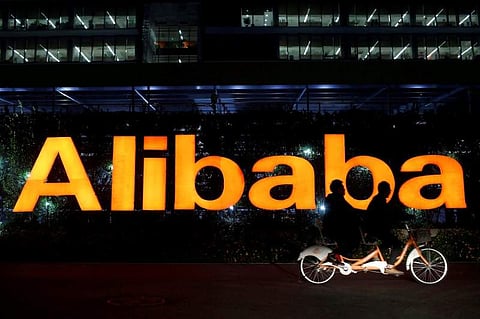 People ride a double bicycle past a logo of The Alibaba Group.(File photo | Reuters)