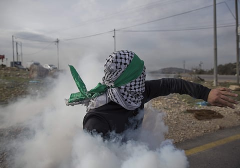 A Palestinian protester returns a teargas canister during clashes with Israeli troops following protests against U.S. President Donald Trump's decision to recognize Jerusalem as the capital of Israel, at the outskirts of the West Bank city of Bir Zeit, Tu