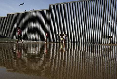 The border structure separating San Diego from Tijuana, Mexico, reflects as people walk along the beach Wednesday, Feb. 1, 2017, in Tijuana. (Photo | AP)