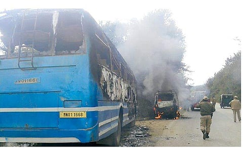 Police personnel walk near a bus and a car set afire by supporters of a bandh called by United Naga Council, at Senapati in Manipur. | Express File Photo