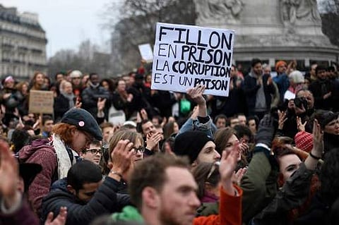 A demonstrator holds a placard reading 'Fillon to prison, corruption is a poison' during a rally to protest against the corruption of the elected representatives in place de la Republique, in Paris, on February 19. (Photo | AFP)