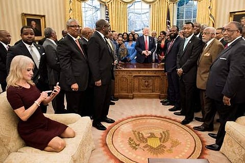 Counselor to the President Kellyanne Conway (L) checks her phone after taking a photo as US President Donald Trump and leaders of historically black universities and colleges pose for a group photo in the Oval Office of the White House before a meeting wi
