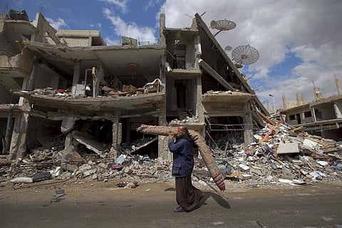 A Syrian man carries a carpet through a devastated part of the town of Palmyra as families load their belongings onto buses in the central Homs province in Syria (File Photo | AP)