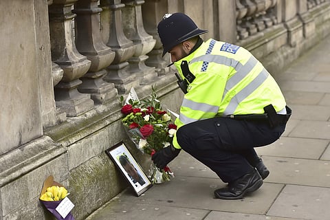 A police officer places flowers and a photo of fellow police officer Keith Palmer, who was killed in yesterdays attack, on Whitehall near the Houses of Parliament in London. (Photo | AP)
