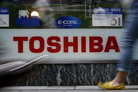 Pedestrians walk past a logo of Toshiba Corp outside an electronics retailer in Tokyo, Japan. | Reuters