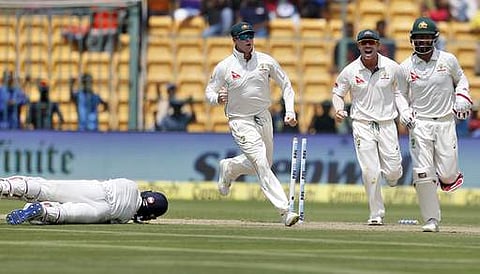 Australia's captain Steven Smith, left, celebrates with teammates Matthew Wade, right, and David Warner the dismissal of India's Ajinkya Rahane, on ground, during the first day of their second test cricket match in Bangalore, India, Saturday, March 4, 201