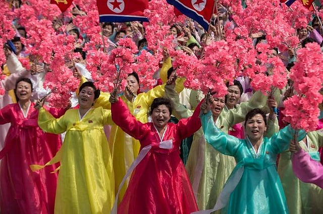 Women wearing traditional Korean dress wave flowers and shout slogans as they pass North Korea's leader Kim Jong-Un during a mass rally. | AFP