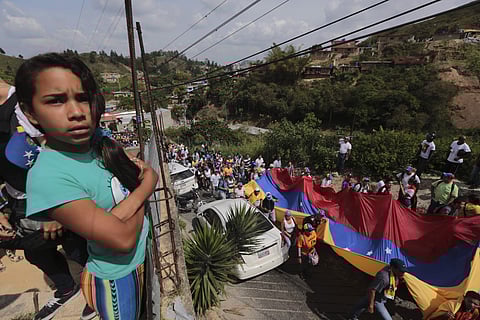 A girl stands on the roof of her house as opponents of President Nicolas Maduro march to the Ramo Verde military prison in Los Teques, outskirts of Caracas, Venezuela, Friday, April 28, 2017. | AP