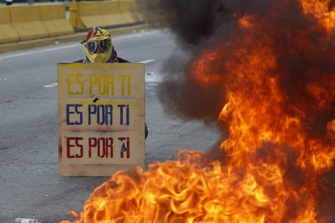 A demonstrator hols a sign that doubles a shield that reads in Spanish 'It's for you,' during a national sit-in against President Nicolas Maduro, in Caracas, Venezuela, Monday, May 15, 2017. Opposition leaders are demanding immediate presidential election