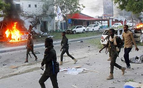Security troops walk past burning cars after a fatal car bomb attack on a restaurant in Mogadishu, Somalia, on Monday, May, 8, 2017.