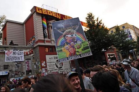 A demonstrator holds a poster with a photo of German Chancellor Angela Merkel and the writing 'festival of democracy with special guests' as a dancing protest against the G-20 summit passes by the Rote Flora squat in Hamburg, northern Germany, Wednesday, 
