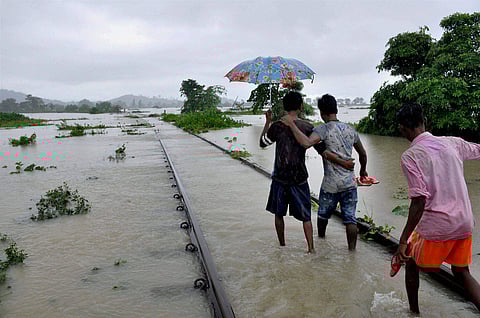 People walking on the flooded railway tracks at Jokhalabandha in Nagaon district of Assam on Monday. | PTI