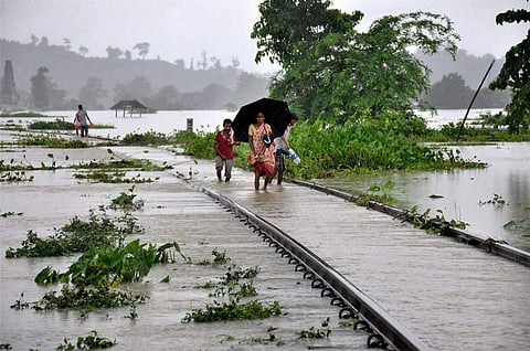 People walking on the flooded railway tracks at Jokhalabandha in Nagaon district of Assam on Monday. | PTI