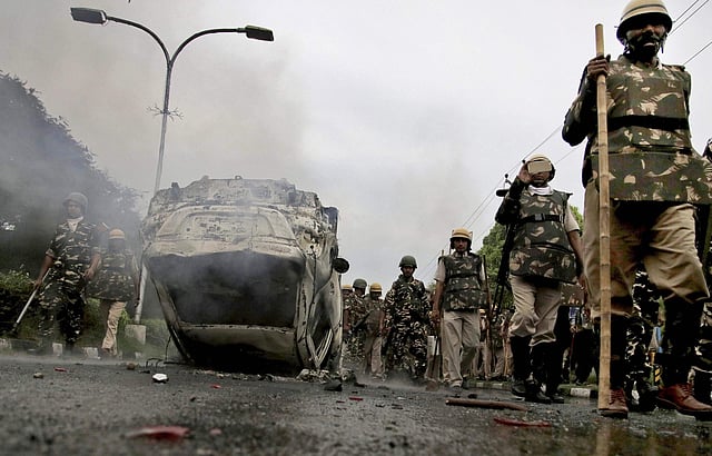 Security personnel walk past a vehicle burnt in the violence that followed Dera Sacha Sauda chief Gurmeet Ram Rahim Singh's conviction by a CBI court in Panchkula on Friday. (Photo | PTI)