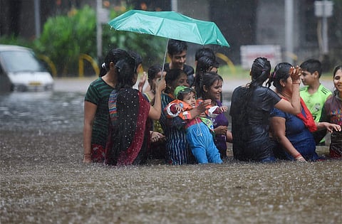 People walk through a flooded street during heavy rains in Mumbai on Tuesday. | PTI