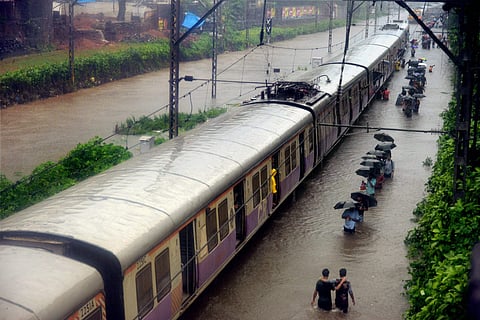 Commuters walk through rain waters along a local train after heavy rains lashed Mumbai on Tuesday. | PTI