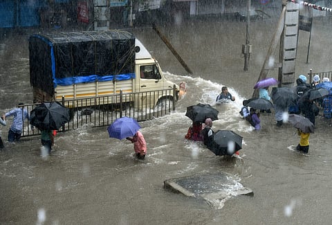 People walk through flooded street during heavy rain showers in Mumbai on Tuesday. | PTI