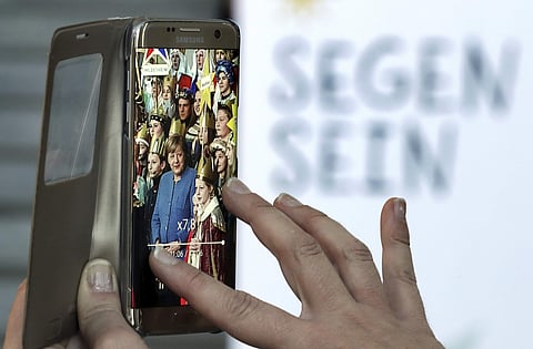 German chancellor Angela Merkel, center, is seen on a smartphone screen as the sings with carolers during a reception for carol singers from all over Germany at the chancellery in Berlin, Germany, Monday, Jan. 8, 2018. Words in German read: 'Be A Blessing