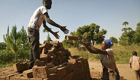 In this photo taken Wednesday, Dec. 13, 2017, Jackline Akot, 36, who was abducted by the Lord's Resistance Army (LRA) as a teenager and had two children before escaping, stacks the bricks that she and her family make in Laliya Oguru village, near Gulu, in